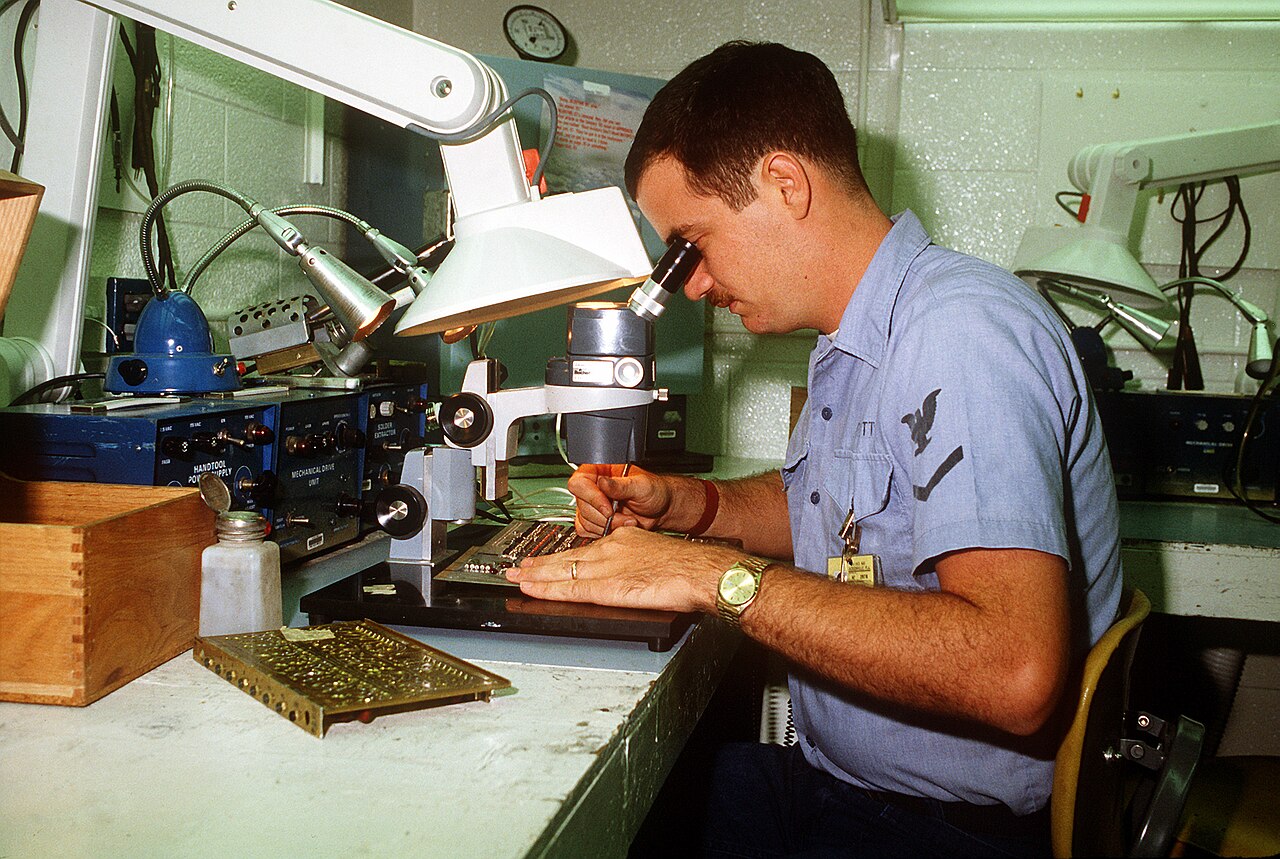 An electronics technician examining a printed circuit board at a workbench