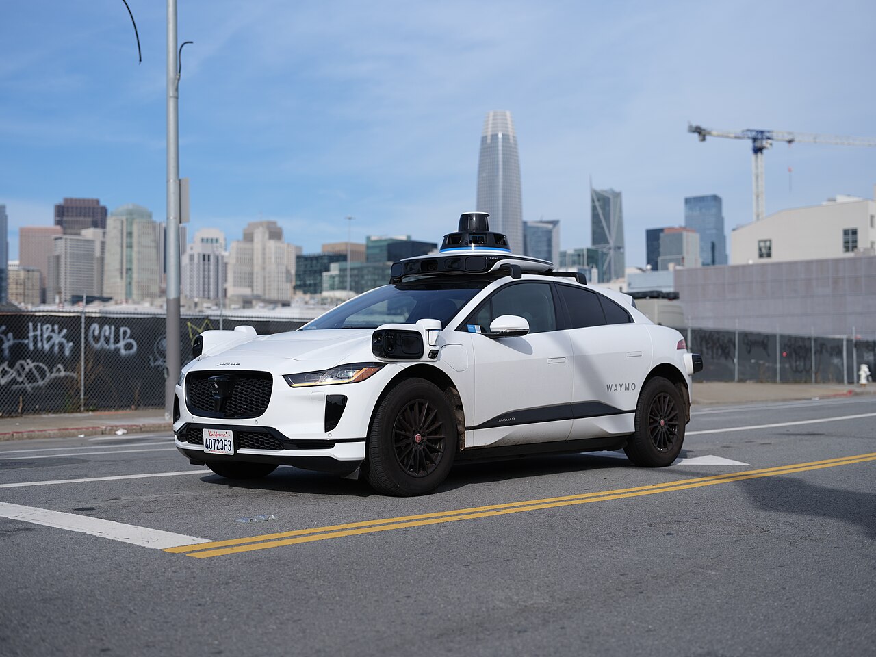 A white Waymo Jaguar I-Pace with roof-mounted sensors on a San Francisco street in 2023