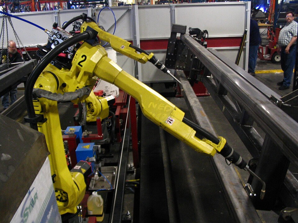 Yellow FANUC industrial welding robots beside metal workpieces