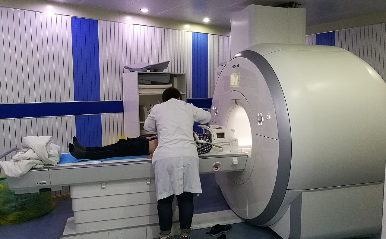 A clinician positions a patient on the table of a Siemens Magnetom Aera MRI scanner; faces are obscured.