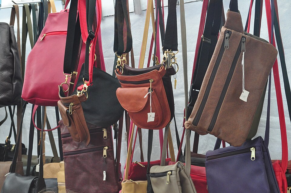 Red, brown, black and purple handbags and pocketbooks hang from a sales rack.
