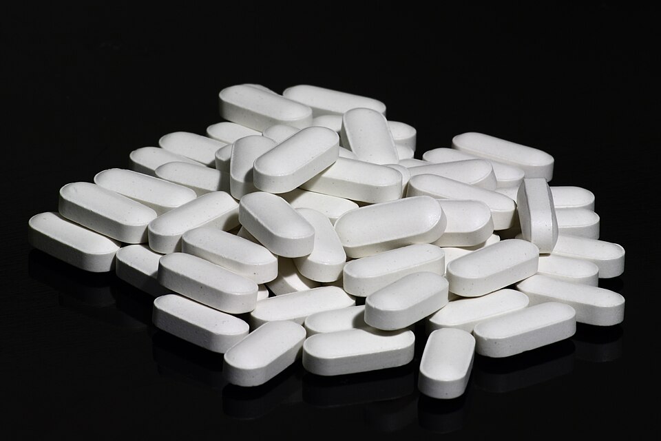 White oblong calcium and vitamin D supplement tablets lie on a black reflective surface.