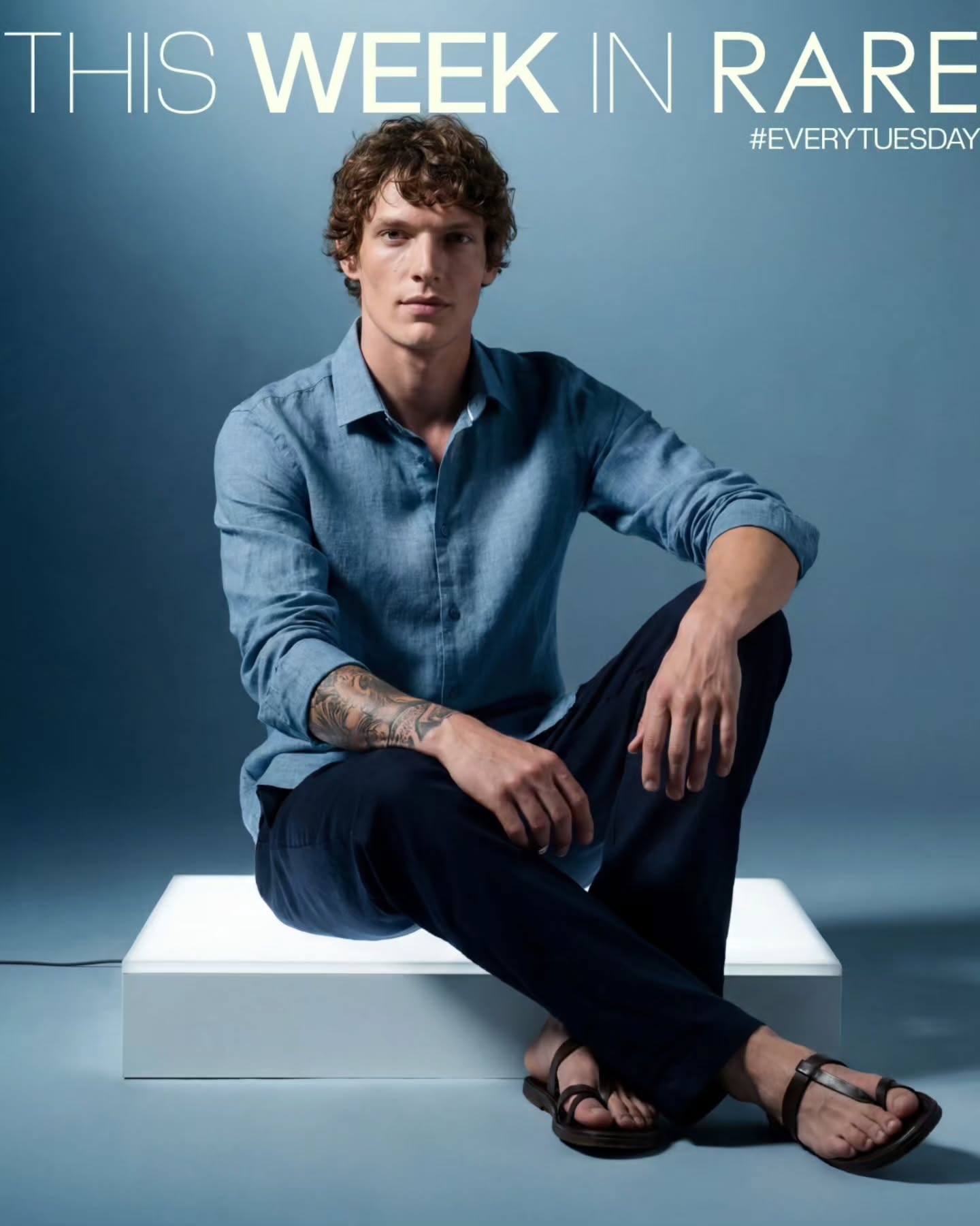 Rare Rabbit campaign image showing a seated figure in a lighter blue shirt against a blue backdrop.
