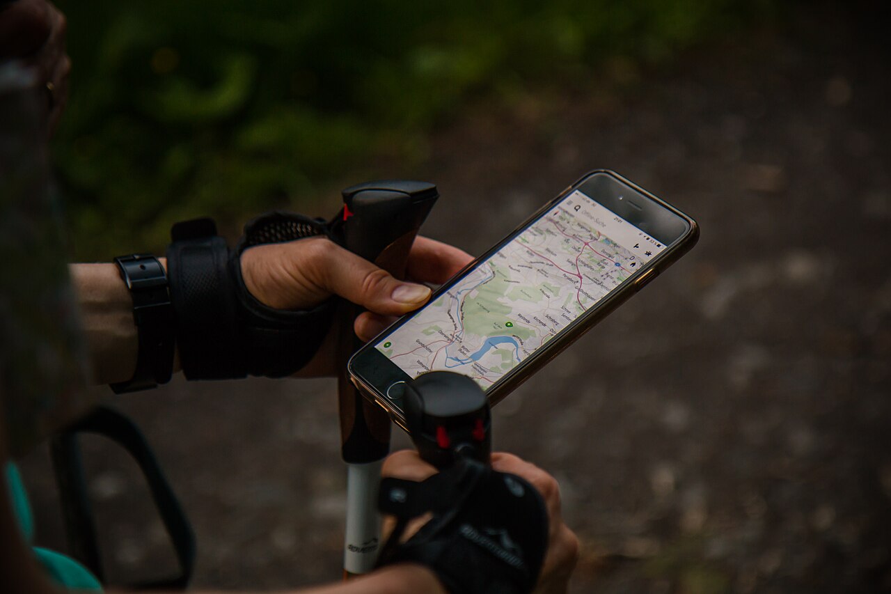 A Nordic walker holding a smartphone beside a walking pole