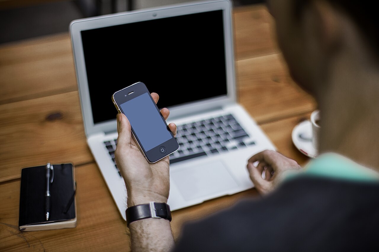 A person using a smartphone beside an open laptop